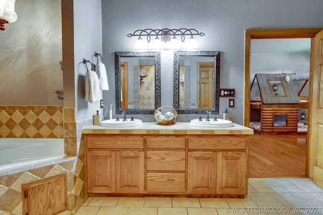 bathroom with tile floors, tiled tub, large vanity, and double sink