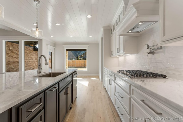 kitchen featuring light stone countertops, sink, white cabinets, and custom exhaust hood