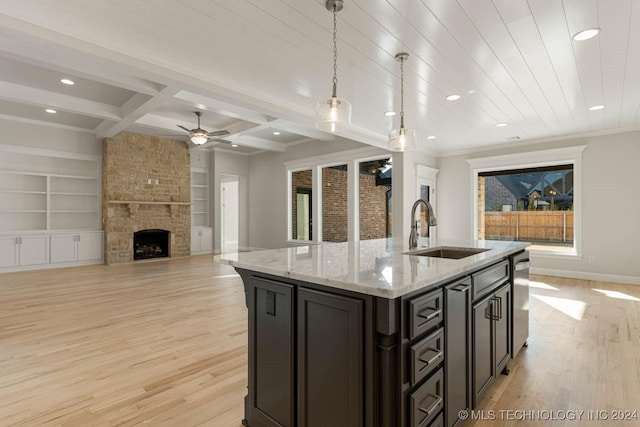 kitchen featuring a kitchen island with sink, sink, hanging light fixtures, light hardwood / wood-style flooring, and light stone countertops