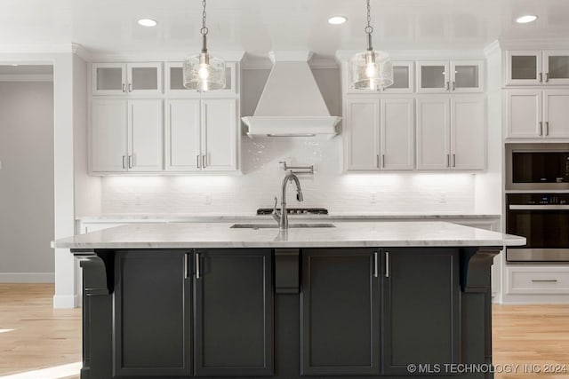 kitchen featuring white cabinets, stainless steel appliances, a center island with sink, and custom exhaust hood