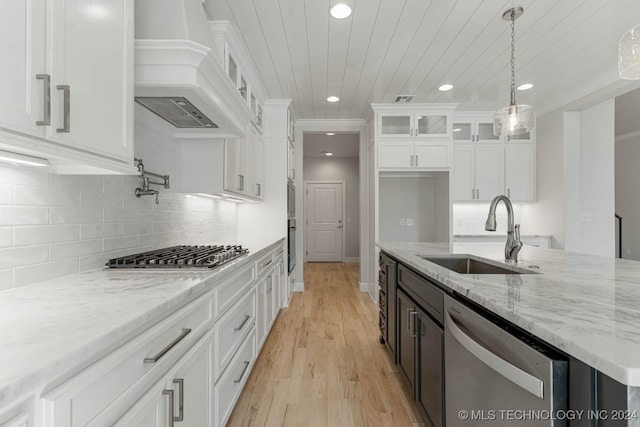 kitchen with custom exhaust hood, white cabinets, sink, decorative light fixtures, and stainless steel appliances