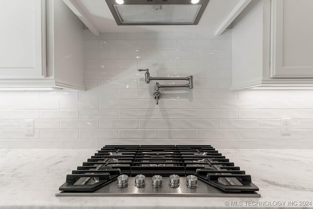 interior details featuring decorative backsplash, white cabinetry, light stone counters, and stainless steel gas cooktop