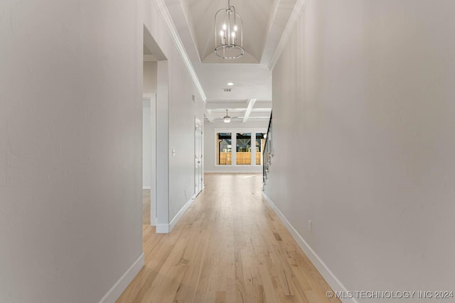 hallway with coffered ceiling, light hardwood / wood-style floors, ornamental molding, and an inviting chandelier