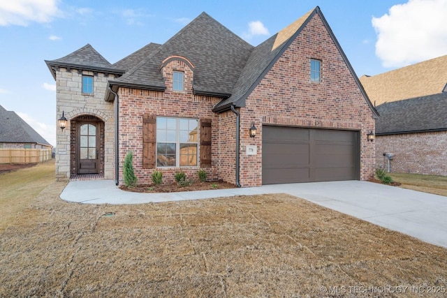 french provincial home featuring driveway, stone siding, a shingled roof, and brick siding