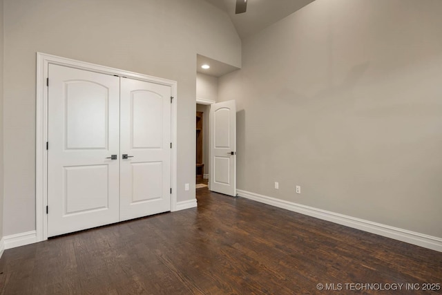 unfurnished bedroom with dark hardwood / wood-style floors, high vaulted ceiling, a closet, and ceiling fan