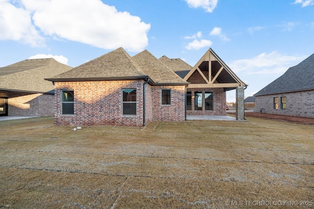 rear view of property with a patio, brick siding, roof with shingles, and a lawn