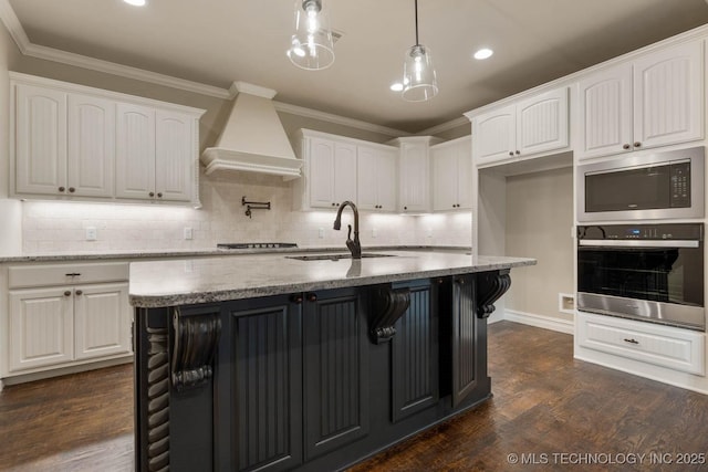 kitchen featuring sink, light stone counters, premium range hood, white cabinets, and appliances with stainless steel finishes