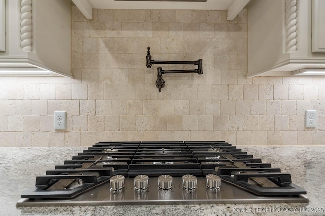 room details featuring decorative backsplash, light stone counters, and stainless steel gas cooktop