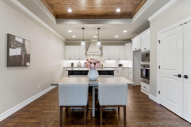 kitchen featuring a raised ceiling, a kitchen island, light countertops, premium range hood, and white cabinetry