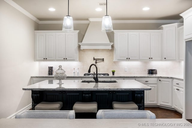 kitchen with light stone counters, pendant lighting, white cabinets, and a center island with sink