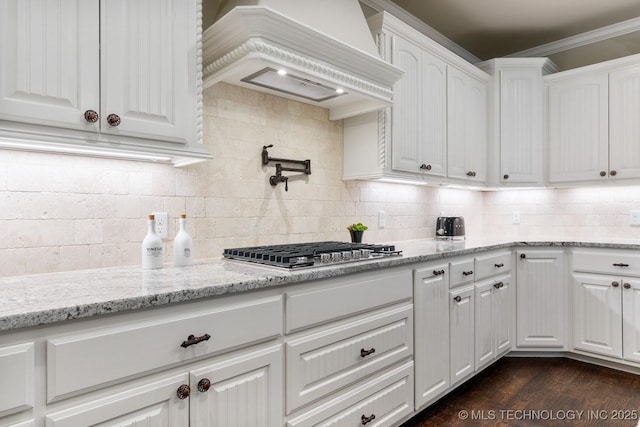 kitchen featuring tasteful backsplash, light stone counters, white cabinetry, premium range hood, and stainless steel gas cooktop