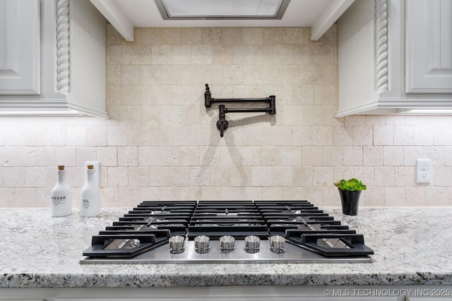 details with tasteful backsplash, stainless steel gas cooktop, white cabinets, and light stone counters