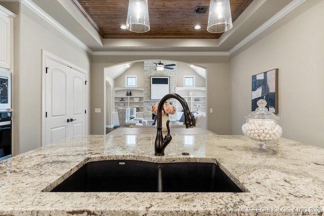 kitchen with arched walkways, a raised ceiling, wood ceiling, a fireplace, and a sink