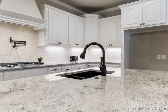 kitchen featuring light stone countertops, crown molding, white cabinetry, stainless steel gas cooktop, and a sink