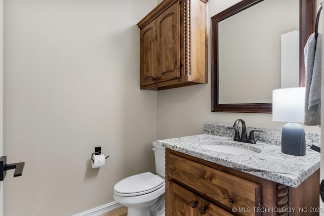 half bathroom with toilet, baseboards, and vanity