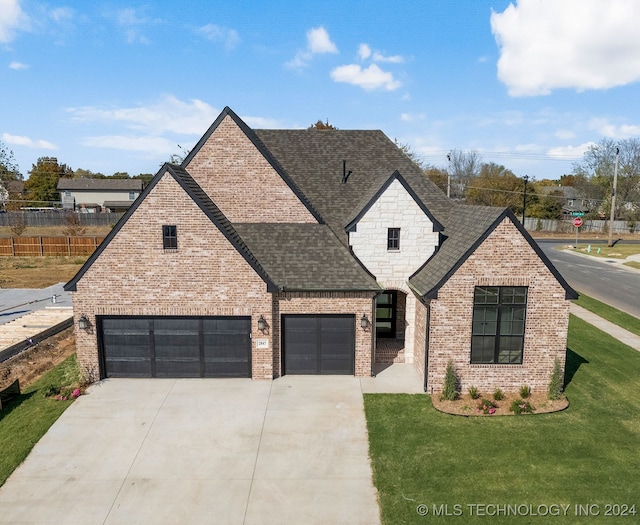 french country inspired facade featuring driveway, brick siding, a front lawn, and roof with shingles