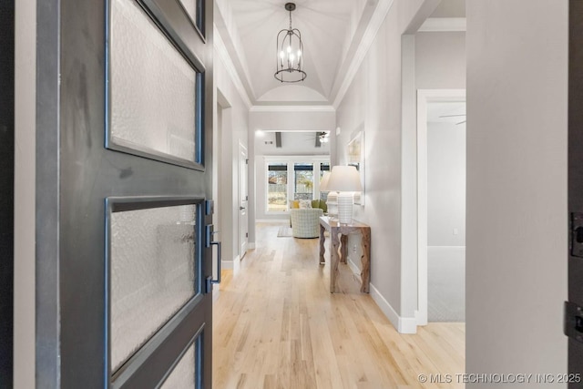 hall featuring a chandelier, light wood-type flooring, baseboards, and crown molding