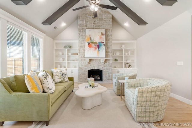 living area featuring light wood finished floors, baseboards, a ceiling fan, a stone fireplace, and built in shelves