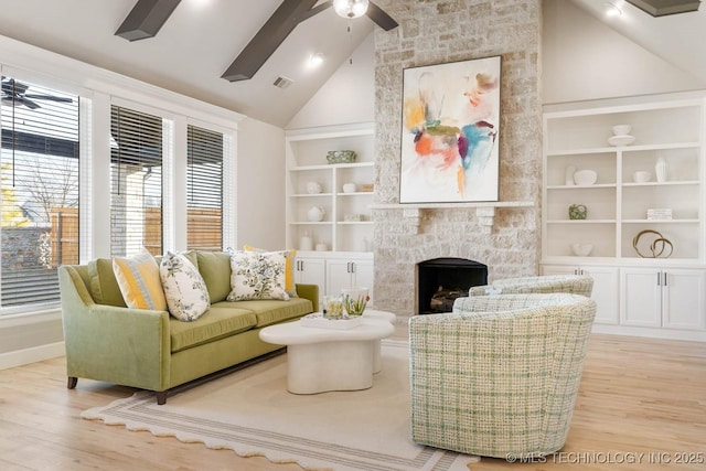 living area with light wood finished floors, built in features, visible vents, a ceiling fan, and a fireplace