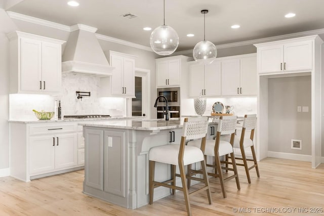 kitchen featuring white cabinets, an island with sink, custom exhaust hood, stainless steel appliances, and pendant lighting