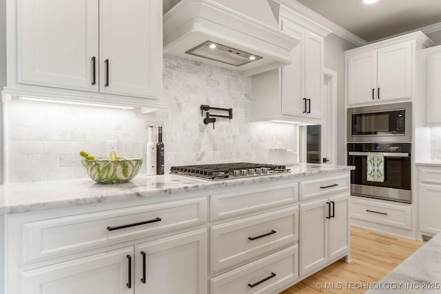 kitchen featuring tasteful backsplash, light stone countertops, custom exhaust hood, stainless steel appliances, and white cabinetry