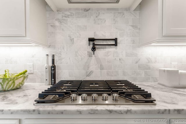 interior details featuring stainless steel gas stovetop, light stone counters, white cabinets, and decorative backsplash