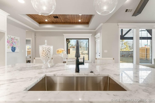 kitchen with visible vents, a tray ceiling, light stone counters, and a sink