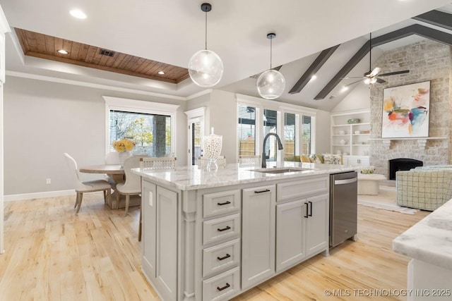 kitchen with built in features, a center island with sink, white cabinets, a sink, and light stone countertops