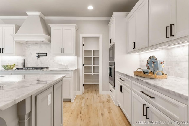 kitchen featuring custom range hood, light stone counters, stainless steel appliances, crown molding, and white cabinetry