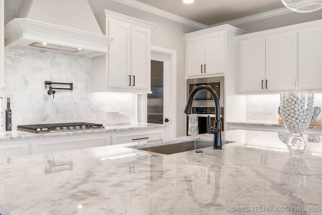 kitchen with a sink, white cabinetry, ornamental molding, light stone countertops, and custom range hood