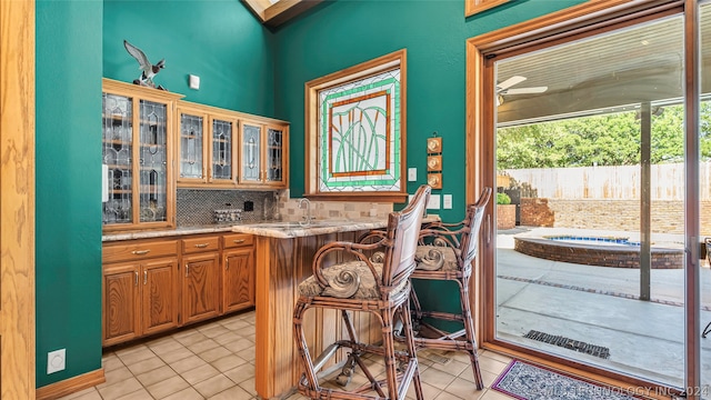 kitchen featuring light stone countertops, light tile flooring, tasteful backsplash, and a kitchen bar