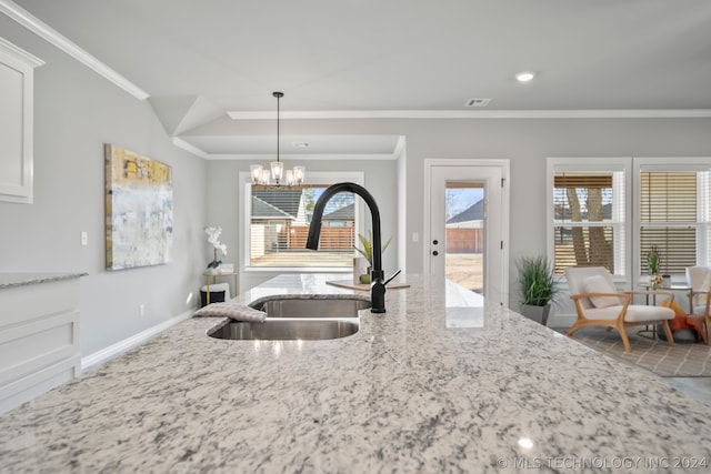 kitchen with sink, white cabinets, ornamental molding, and an inviting chandelier