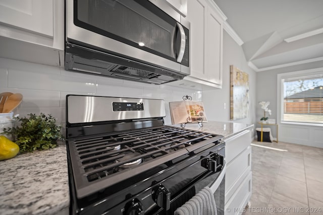 kitchen featuring appliances with stainless steel finishes, white cabinets, light stone counters, backsplash, and light tile floors