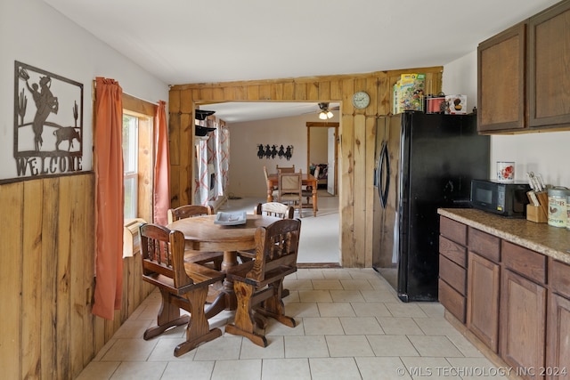 dining space with wooden walls, ceiling fan, and light tile floors