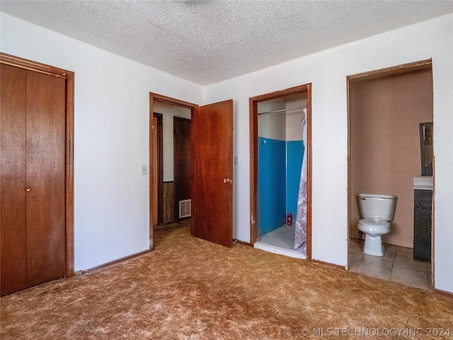 unfurnished bedroom featuring ensuite bathroom, light carpet, and a textured ceiling