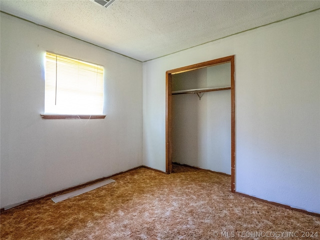 unfurnished bedroom featuring a textured ceiling, light colored carpet, and a closet