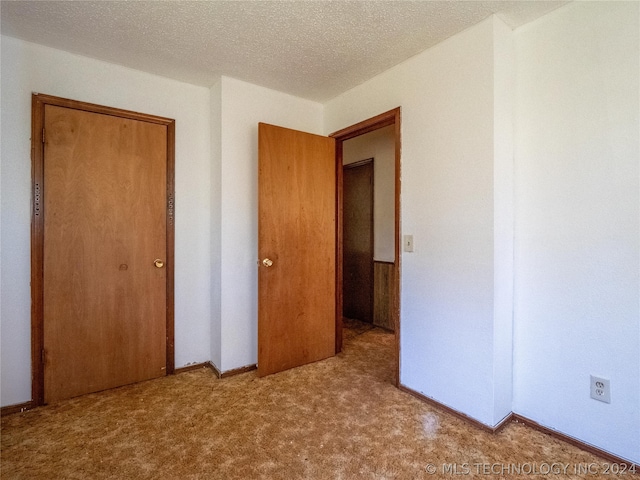 unfurnished bedroom featuring a textured ceiling, light colored carpet, and a closet