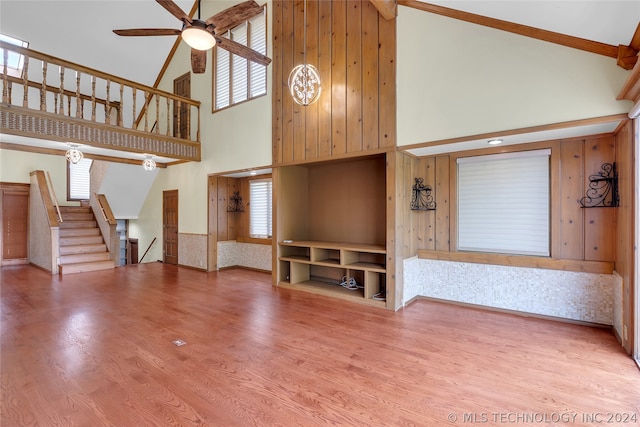 unfurnished living room featuring hardwood / wood-style floors, ceiling fan, wood walls, and high vaulted ceiling