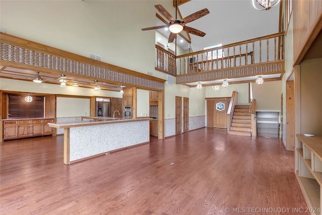 unfurnished living room with hardwood / wood-style flooring, ceiling fan, a towering ceiling, and sink