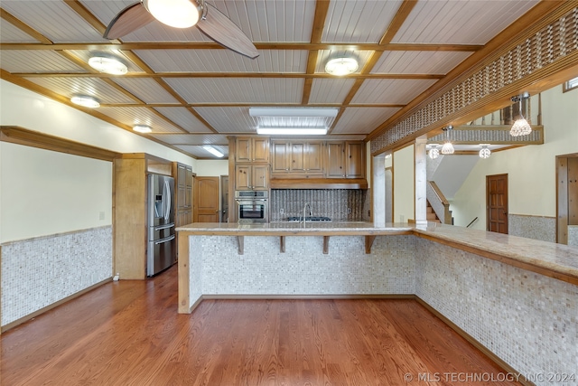 kitchen featuring a kitchen bar, appliances with stainless steel finishes, kitchen peninsula, brick wall, and wood-type flooring