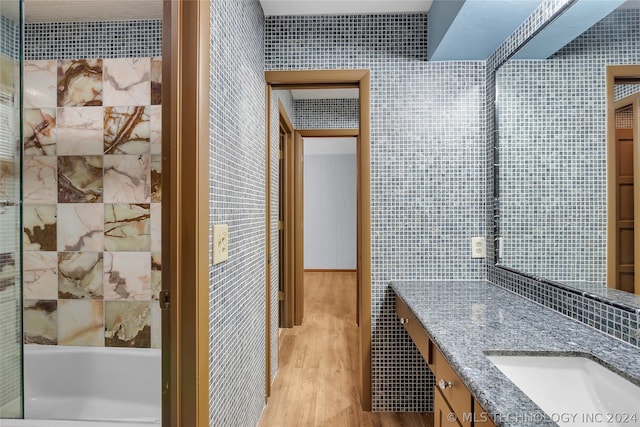 bathroom with a bathtub, vanity, hardwood / wood-style flooring, and tile walls