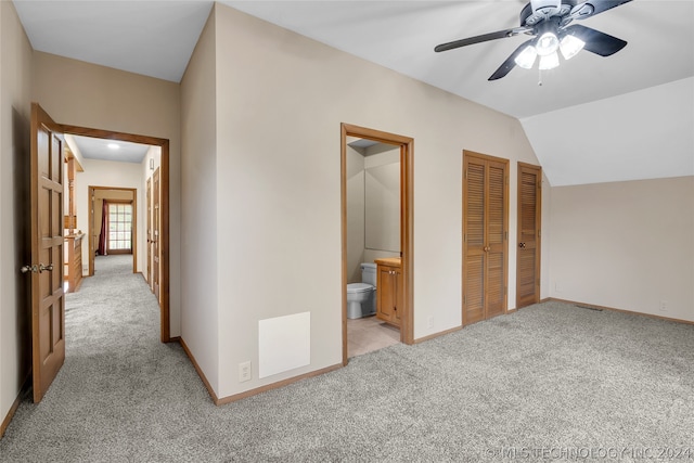 unfurnished bedroom featuring ceiling fan, ensuite bathroom, vaulted ceiling, light carpet, and two closets