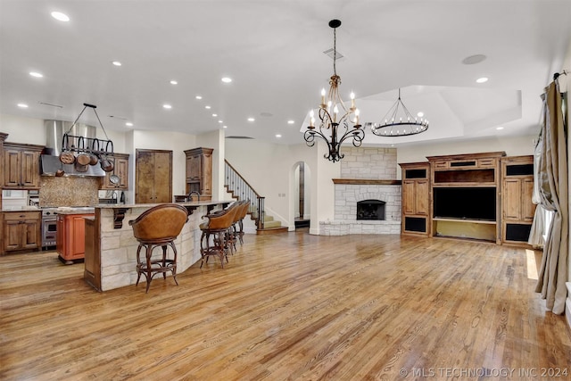 kitchen featuring a kitchen breakfast bar, light wood-type flooring, ventilation hood, decorative light fixtures, and a stone fireplace