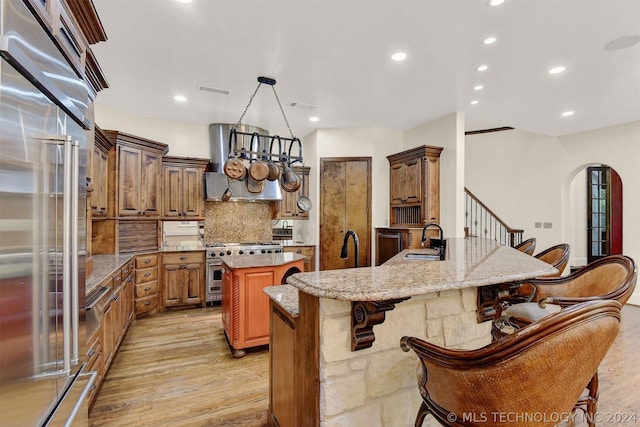 kitchen featuring high quality appliances, light wood-type flooring, a kitchen bar, kitchen peninsula, and extractor fan