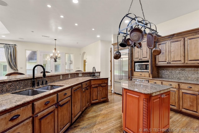 kitchen with light stone countertops, a center island, built in appliances, and sink