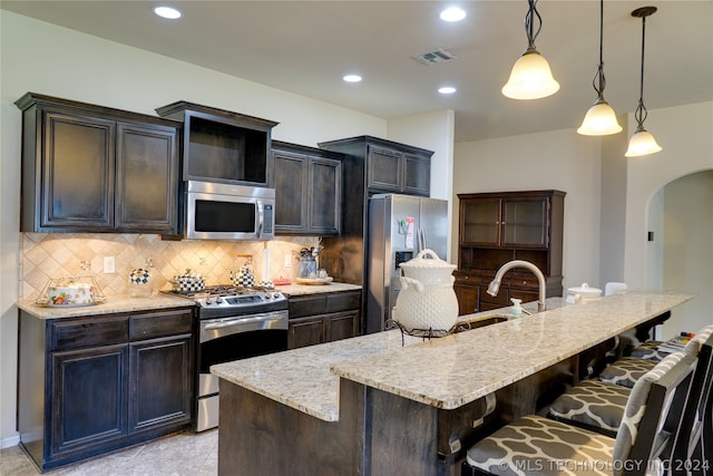 kitchen featuring stainless steel appliances, a kitchen breakfast bar, an island with sink, decorative light fixtures, and decorative backsplash