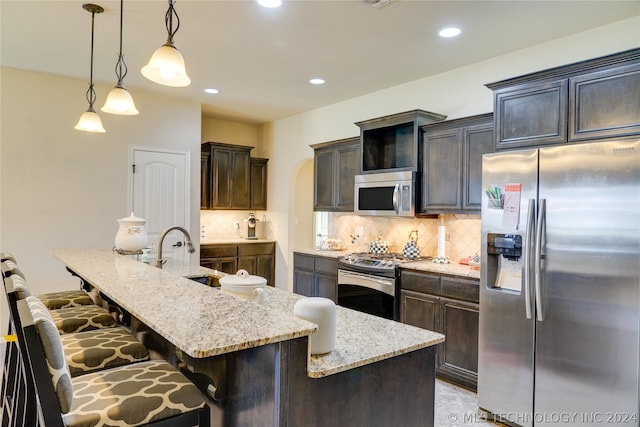 kitchen featuring backsplash, an island with sink, hanging light fixtures, and appliances with stainless steel finishes