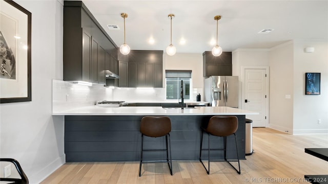 kitchen featuring kitchen peninsula, stainless steel refrigerator with ice dispenser, light wood-type flooring, and decorative light fixtures