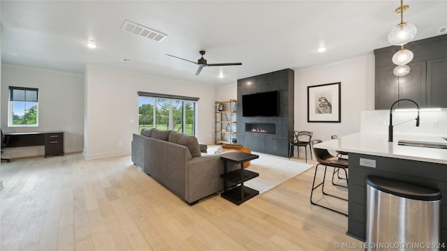 living room with ornamental molding, ceiling fan, sink, a tile fireplace, and light hardwood / wood-style flooring