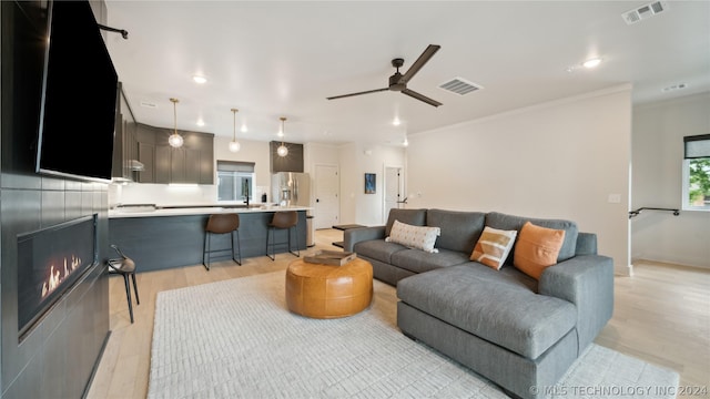 living room with light hardwood / wood-style flooring, ceiling fan, and crown molding